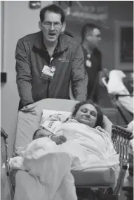  ?? MICHAEL SEARS / MILWAUKEE JOURNAL SENTINEL ?? John Melara wheels patient Ricky Myers back to the emergency department while singing to her at Aurora West Allis Medical Center.