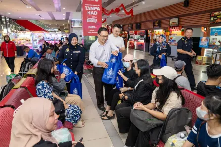  ?? — Photo by Chimon Upon ?? Chong distribute­s goodie bags to passengers waiting to depart by bus flanked by Noraini and Lam.