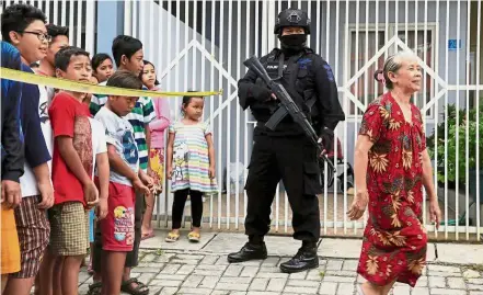  ?? — Reuters ?? Terror at home: A policeman standing guard during a raid at the home of a suspected terrorist as people watch at the Medokan Ayu area in Surabaya.