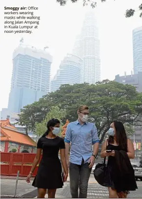  ??  ?? Smoggy air: O ce workers wearing masks while walking along Jalan Ampang in Kuala Lumpur at noon yest a .