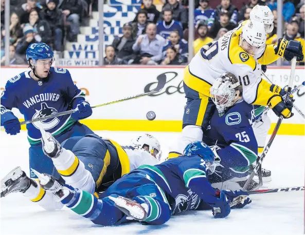  ?? — DARRYL DYCK/THE CANADIAN PRESS ?? Vancouver’s Derrick Pouliot, kneeling, follows the puck after Ben Hutton, front right, scoops it off the goal-line behind goalie Jacob Markstrom, to prevent Nashville’s Austin Watson, second left, Colton Sissons (10) and Mike Fisher, rear, from scoring...