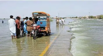  ?? Picture: REUTERS/AKHTAR SOOMRO ?? UNDER WATER: Displaced people stand on a flooded highway after rains during the monsoon season in Sehwan, Pakistan, in September 2022.