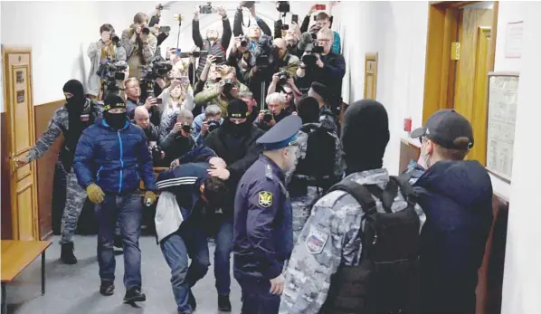  ?? — AFP ?? A man suspected of taking part in the attack of a concert hall is escorted by Russian law enforcemen­t officers prior to his pre-trial detention hearing at the Basmanny District Court in Moscow.