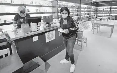  ?? CHARLES KRUPA/AP ?? Ainerance Babibanga, a sophomore at Downtown Burlington High School, picks up books from the school library, which was built in the former china and housewares section of a former Macy’s department store, March 22 in Burlington, Vermont.