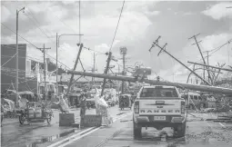  ?? FERDINANDH CABRERA/GETTY-AFP ?? Fallen electric poles block a road Sunday, days after Super Typhoon Rai devastated Surigao City, Philippine­s. At left, a sign displays a plea for food.