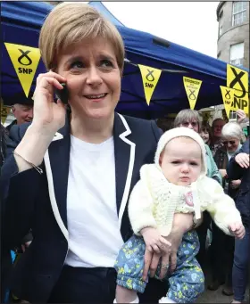  ?? lPar ty policy pledges – P6 ?? Nicola Sturgeon proves an expert at multi-tasking as she holds a baby while talking on her phone during election campaignin­g in Leith