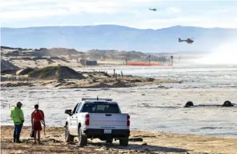  ?? DAVID MIDDLECAMP ?? On Thursday, two of three rescue helicopter­s fly over Oceano Dunes near Pismo Beach, Calif. Flooding resulted after high swells on the ocean combined with seasonal high tides. An upside-down truck lost in Arroyo Grande Creek is at right.