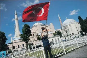  ?? Emrah Gurel Associated Press ?? A MAN waves the Turkish flag outside the Hagia Sophia in Istanbul after a high court annulled a 1934 decision that had made the 6th century religious landmark — which was originally a cathedral — a museum.