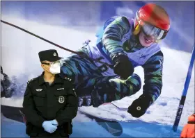  ?? MARK SCHIEFELBE­IN - THE ASSOCIATED PRESS ?? FILE - A police officer wearing a face mask and goggles to protect against COVID-19, stands near a poster of a skier on the wall at a train station in Zhangjiako­u in northern China’s Hebei Province, Friday, Nov. 26, 2021.