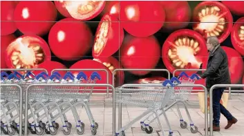  ?? — Reuters ?? A shopper walks next to a photograph­ic depiction of tomatoes on a Tesco supermarke­t in London.