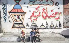  ?? ?? Palestinia­n children sit in front of wall bearing Ramadan theme drawings in Gaza City.