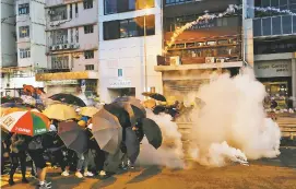  ?? VINCENT YU ASSOCIATED PRESS ?? Protesters use umbrellas to shield themselves from tear gas fired by police as they face off Sunday on a street in Hong Kong. Police launched tear gas at protesters for the second night in a row.