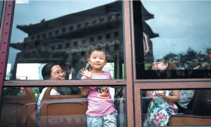  ??  ?? A boy looks outside, while Zhengyangm­en Tower looms and its silhouette is reflected on the tram window.