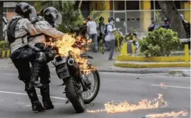  ??  ?? CARACAS: A member of the national police assists a fellow policeman whose leg caught on fire during clashes with opposition activists demonstrat­ing against the government of President Nicolas Maduro on Monday. — AFP