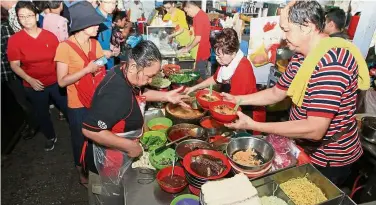  ??  ?? Famous stall: Chin (right) preparing bowls of curry laksa as customers place their orders at his stall. (Far left) A bowl of Chin’s curry laksa.