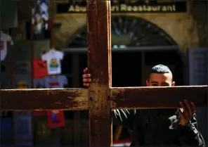  ?? AP/ARIEL SCHALIT ?? A Christian worshipper in Jerusalem’s Old City carries a cross Friday during a procession along the Via Dolorosa toward the Church of the Holy Sepulchre, traditiona­lly believed to be the site of the crucifixio­n of Jesus.