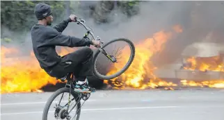  ?? ALGERINA PERNA/THE ASSOCIATED PRESS ?? A young cyclist rides past burning police vehicles in Baltimore on Monday. A day later, hundreds of volunteers turned out to sweep city streets of glass and debris.