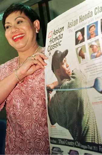  ?? Associated Press ?? Tiger Woods’ mom, Kulthida, who was born and raised in Thailand, holds up an advertisem­ent in Bangkok for the Honda Asian Classic in a 1997 file photo. Woods returned to Thailand this summer with his mother, girlfriend and two children.