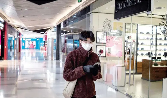  ?? Agence France-presse ?? ↑
A man, wearing a protective face mask, goggles and gloves walks in a deserted shopping mall in Beijing on Monday.