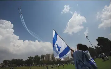  ?? (Marc Israel Sellem/The Jerusalem Post) ?? GIRLS WAVE a flag as planes fly overhead in the traditiona­l air display during Independen­ce Day celebratio­ns in Jerusalem’s Sacher Park on Tuesday.