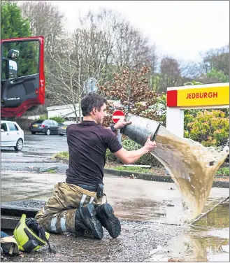  ??  ?? WASH OUT: A firefighte­r in Jedburgh clears up after heavy rain flooded key routes into the town.