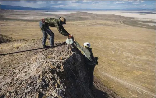  ?? (AP/The Deseret News/Spenser Heaps) ?? Hawkwatch Internatio­nal research associate Dustin Maloney (right) hands a bagged golden eagle nestling to field biologist Jayden Skelly on May 19 after Maloney removed it from its nest on a cliff in a remote area of Box Elder County, Utah.