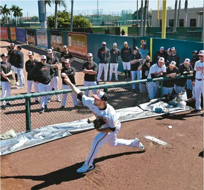  ?? KENNETH K. LAM/STAFF PHOTOS ?? The Orioles gather to watch starting pitcher Corbin Burnes warm up in the bullpen before Saturday’s Grapefruit League opener at Ed Smith Stadium in Sarasota, Florida.