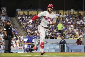  ?? MARK J. TERRILL — THE ASSOCIATED PRESS ?? Philadelph­ia Phillies’ Bryce Harper, right, gestures toward his dugout as he heads to first after hitting a three-run home run as Los Angeles Dodgers catcher Austin Barnes, center, kneels at first as home plate umpire Adrian Johnson watches during the third inning of a baseball game on Saturday night.