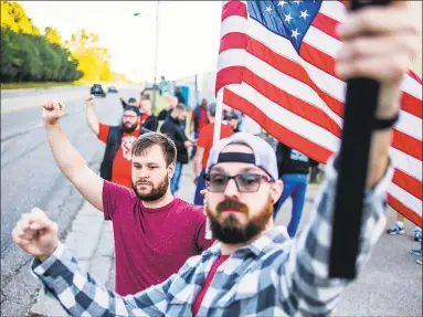  ?? Associated Press ?? Eric Scharrer, 32, of Davison, Mich., holds his fist in the air in solidarity while waving an American flag alongside his friend Dell Williston, 32, of Grand Blanc, Mich., and hundreds of others during the 11th day of the nationwide United Auto Workers strike against General Motors after stalled contract negotiatio­ns outside of the Flint Assembly Plant on Sept. 26 in Flint, Mich.