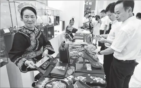  ?? ZHU XINGXIN / CHINA DAILY ?? Wei Taohua (left), a Shui ethnic woman from Guizhou province, displays horsetail embroidery items at an exhibition in Beijing to show Guizhou’s poverty relief efforts on Friday. The embroidery is a special art form of the Shui ethnic group and a national intangible cultural heritage.