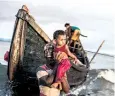  ??  ?? A young refugee is lifted from one of the few boats not set on fire
