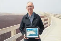  ??  ?? Kevin Sanderson stands along the boardwalk in Prince Edward Island National Park, holding a photo — taken by Don Jardine — of the park’s vulnerable and rare parabolic sand dunes. His family once lived and farmed nearby.