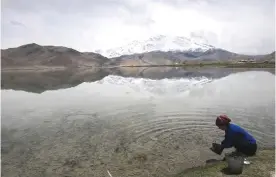  ??  ?? TASHKURGAN: This picture shows a woman collecting water from the Karakul Lake before the Karakorum mountain range next to the China-Pakistan Friendship Highway, near Tashkurgan in China’s western Xinjiang province.—AFP