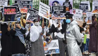  ?? — AFP file photo ?? A policeman stands guard as protesters hold placards during a demonstrat­ion against the government policy of forced cremations of Muslims who died of the Covid-19 coronaviru­s, outside a cemetery in Colombo.