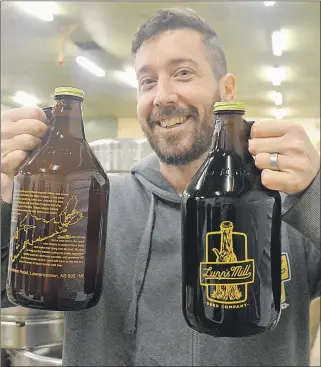  ??  ?? Mark Reid holds up a couple of growlers of Lunn’s Mill Beer Company product during opening day of the new Lawrenceto­wn brewery on March 2. He is partners with Sean Ebert, Chantelle Webb and Chad Graves.