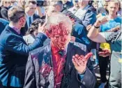  ?? WOJTEK RADWANSKI/GETY-AFP ?? Protesters opposed to the war in Ukraine douse Ambassador Sergey Andreev with red paint Monday at the Soviet Military Cemetery in Warsaw, Poland.