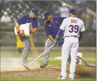  ?? Kathy Willens / Associated Press ?? Heavy rain falls as Mets relief pitcher Edwin Diaz watches groundskee­pers groom the mound with extra dirt during the ninth inning of Thursday’s game against the Cardinals, The game, tied at 4-4, was suspended due to the rain.