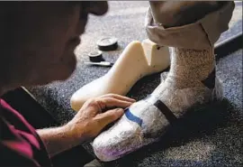  ??  ?? AT HIS WORKSHOP, Randy Merrell inspects the fit of trial boots made from packaging tape on Tom Overton, an attorney from Evergreen, Colo.