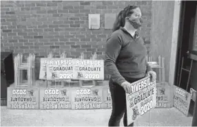  ?? MIKE DE SISTI / MILWAUKEE JOURNAL SENTINEL ?? Riverside University High School physical education teacher Lindsey Gerszewski holds a yard sign to be handed out at Riverside in Milwaukee. While all MPS school buildings are closed for the remainder of the 2019-20 school year because of the COVID-19 pandemic, graduating seniors were able to pick up packets that included their caps, gowns, diploma covers, yearbooks and yard signs. The district will be offering a virtual graduation on its YouTube page.