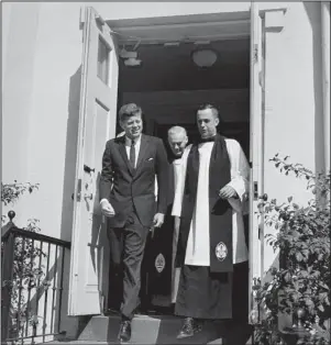  ?? The Associated Press ?? ST. JOHN’S: In this March 10, 1963, file photo, President John F. Kennedy leaves St. John’s Episcopal Church after attending Mass at St. Stephens Roman Catholic Church in Washington. At right is the Rev. John C. Harper, new rector of the church, and at rear is the Rt. Rev. William F. Creighton, Episcopal Bishop of Washington. During his visit to St. John’s, Kennedy signed a prayer book which bears the signatures of all presidents since Herbert Hoover.
