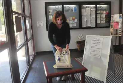  ?? Ernest A. Brown photos ?? Celeste Dyer, Library Director at Cumberland Public Library, brings out an order of books for a library patron at the library Wednesday. The procedure allows for members to call or email their requests for books from the library’s collection, and Dyer will leave them on a table at the entrance to the library in Cumberland. It is one of the many necessary convenienc­es during the coronaviru­s crisis.