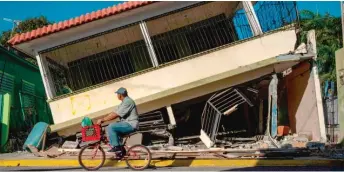  ?? RICARDO ARDUENGO/AFP VIA GETTY IMAGES ?? A man rides his bike past a collapsed house on Jan. 15 in Guanica, Puerto Rico.