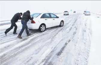  ?? Mark Reis / Associated Press ?? Curtis Hansen (left) and Jeff Malley push a motorist up the icy northbound off-ramp from Interstate 25 to Baptist Road, north of Colorado Springs.