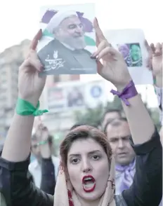  ?? — AFP ?? A supporter of newly re-elected Iranian President Hassan Rouhani holds a placard bearing a portrait of him as she takes to the streets to celebrate his victory in downtown Tehran on Saturday.