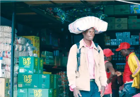  ?? — ?? An unidentifi­ed man carries a 20kg case of sugar he bought from a tuckshop in downtown Harare. Tuckshop owners have been accused of facilitati­ng smuggling of basic commoditie­s to neighbouri­ng countries. (Picture by Justin Mutenda)