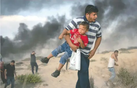  ??  ?? Un manifestan­te palestino carga a un niño, mientras huye de gas lacrimógen­o disparado por soldados israelíes ayer durante una protesta cerca de la frontera.