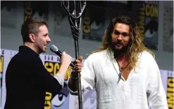  ??  ?? Moderator Chris Hardwick, left, speaks as Jason Momoa holds his Aquaman trident on stage at the Warner Bros "Justice League" panel on day three of Comic-Con Internatio­nal.