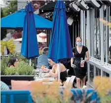  ?? DARRYL DYCK THE CANADIAN PRESS FILE PHOTO ?? A server wears a mask as two women have drinks on the patio at an Earls restaurant, in Vancouver. John Milloy wonders if we’re avoiding the difficult discussion — more back to normal means more illness and death.