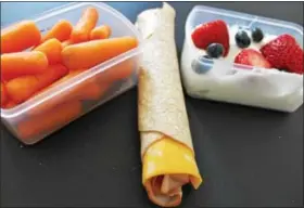  ??  ?? A whole grain wrap with lean turkey along with nonfat Greek yogurt and carrots are displayed. Use individual containers to keep food fresh when packing school lunches.