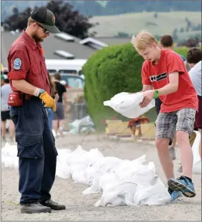  ?? JOE FRIES/Penticton Herald ?? Pen-Hi student Jacob Nickel takes direction Wednesday from Eli Riedl of the BC Wildfire Service, who was guiding constructi­on of a sandbag wall in Red Wing.